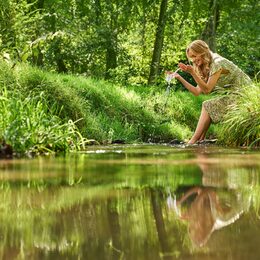 Imagebild Klimaschutzpreis: Frau sitzt im Grünen mit den Füßen in einem Gewässer